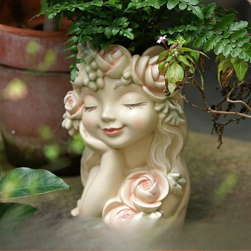 "Rose Muse" resin fairy head planter in Blush Cream — styled with trailing fern plant in a garden setting