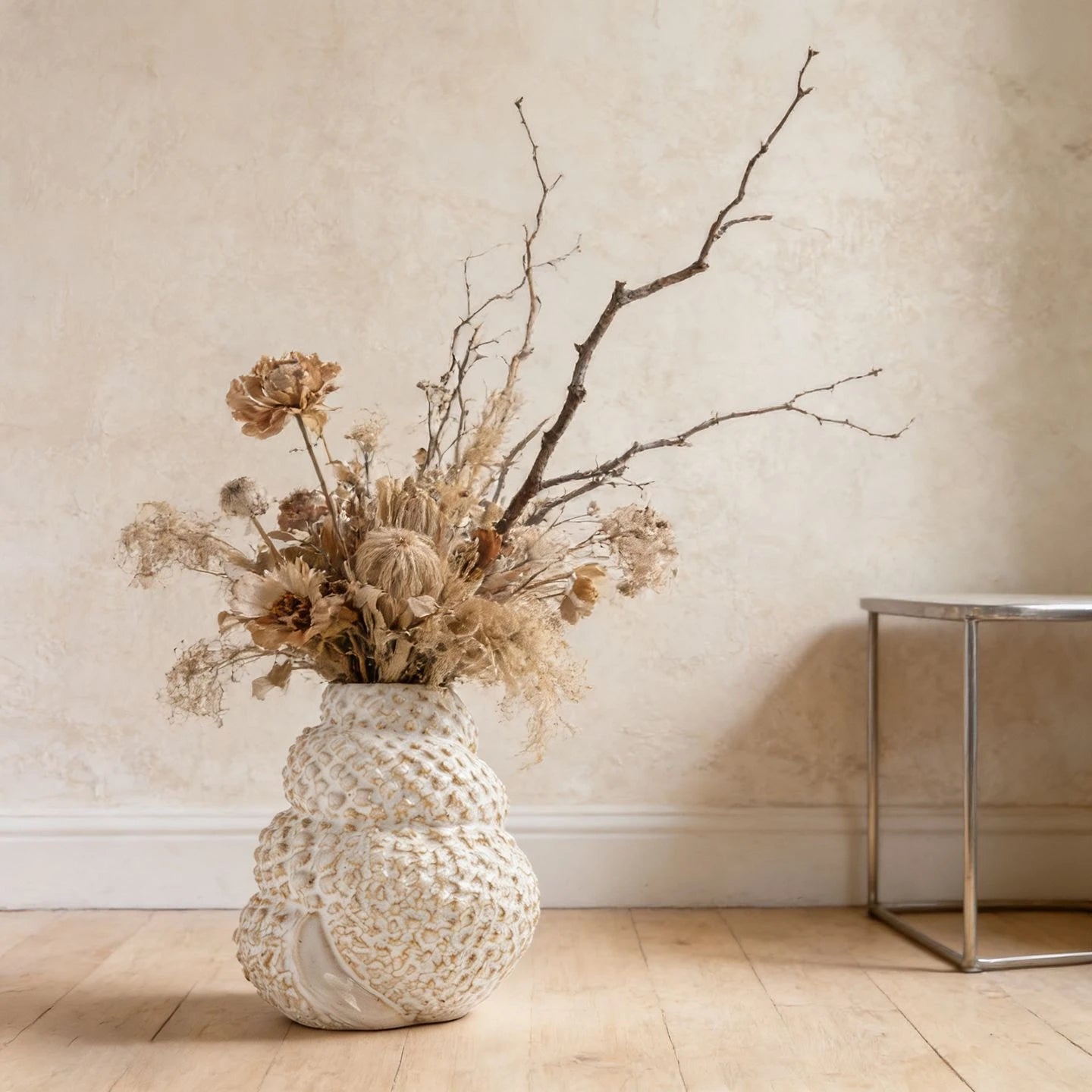 Coral Nest textured ceramic vase styled with dried protea and bare branches on wooden floor, textured wall background