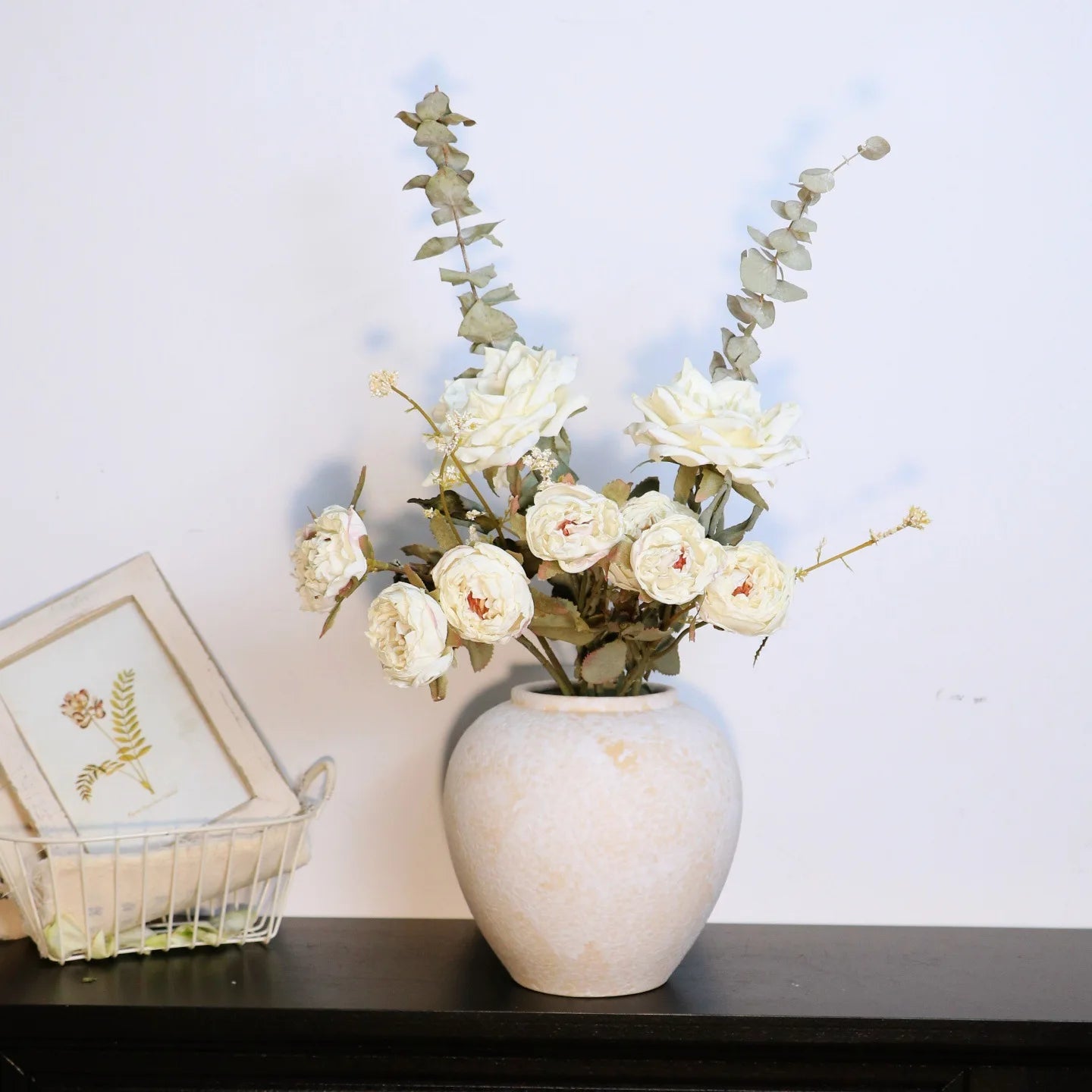 Round Earth ceramic pot vase in Stone Matte finish styled with white roses and eucalyptus on dark shelf, light wall background