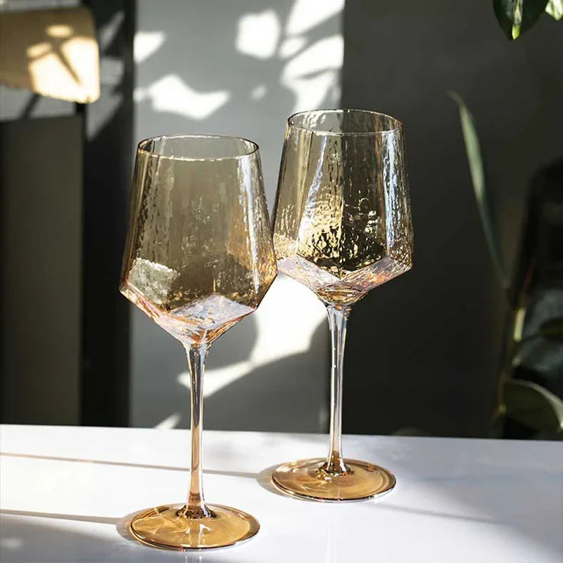 Two iridescent amber crystal wine glasses on a white table, illuminated by sunlight.