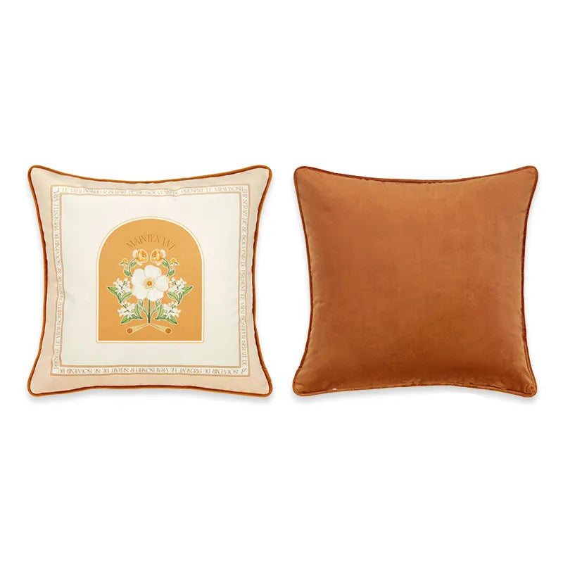 "Maintenant" botanical velvet cushion cover front and back view, cream ground with Latin script border, golden arch framing a white botanical bloom with green foliage, plain caramel velvet reverse with orange piping — CL House Cushions collection