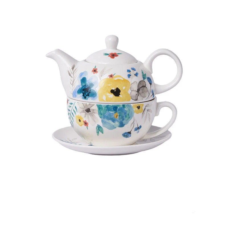 White porcelain tea for one set with watercolour-style blue, yellow and grey flowers, teapot stacked on cup and saucer on white background