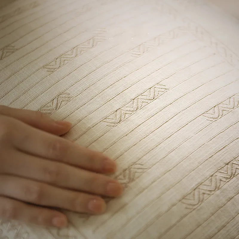 Close-up of a hand gently touching the geometric jacquard weave of an ivory ramie-linen cushion cover, highlighting the intricate texture and artisanal craftsmanship — wabi-sabi handcrafted home decor.