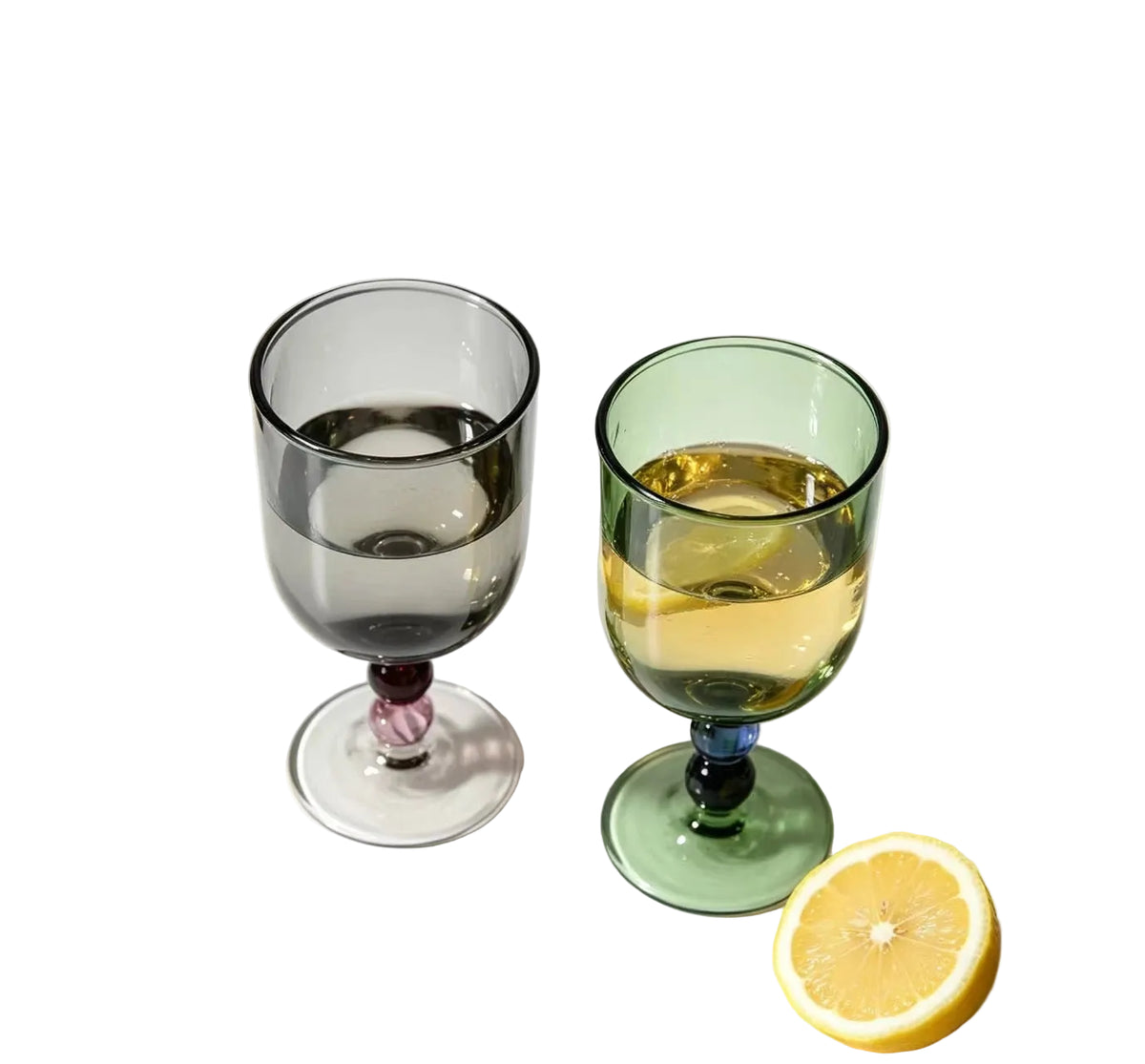 "Chromatic Orb" glass goblets in smoke grey and forest green filled with white wine, on a white background with a halved lemon