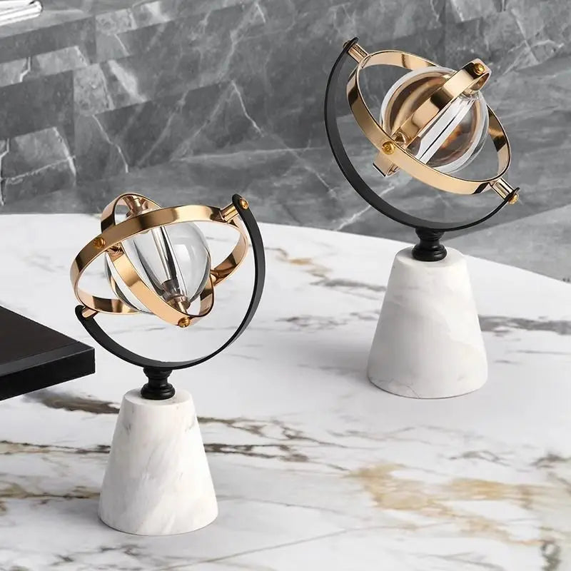 Two decorative marble globes with clear glass spheres and brass and black rings, displayed together on a marble surface