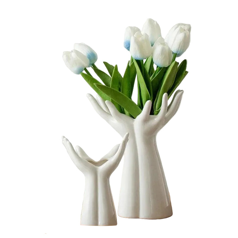 Both sizes of the white ceramic hand vase shown side by side, the smaller empty and the larger holding a bunch of white tulips, on a plain white background