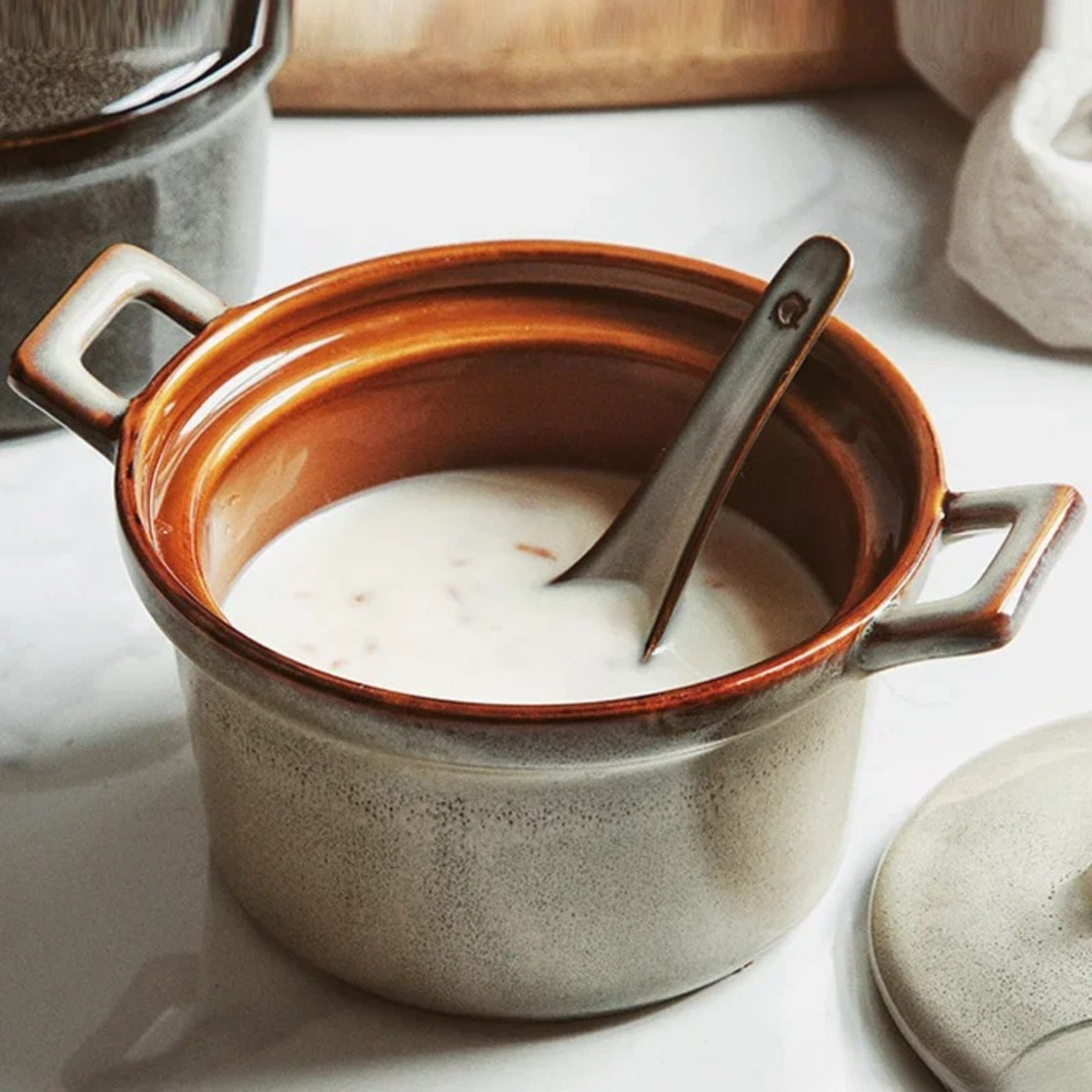 Sand Stone ceramic casserole open without lid, filled with creamy soup and a vintage spoon, amber glazed interior, styled on marble surface with other ceramic pieces in background — Stone Vessel by CL House