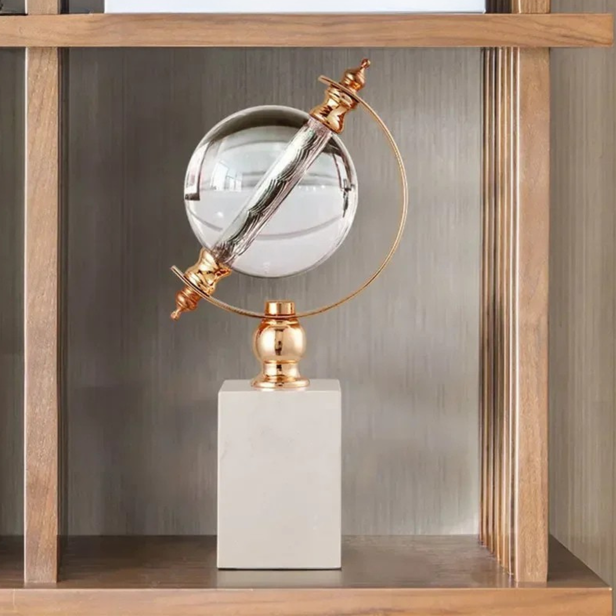 Crystal globe sculpture with gold-plated ring and white marble base, displayed inside a natural wood shelving unit