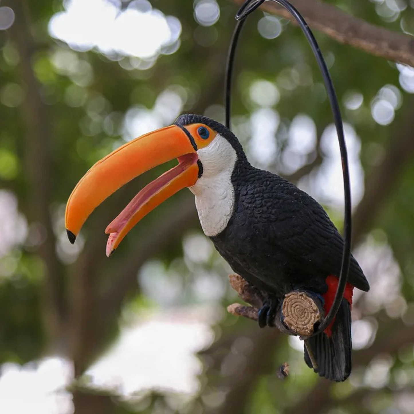 "Wild Perch" hand-painted resin toucan on metal ring hanger, black plumage with vivid orange beak, hanging garden ornament, lush green tree background