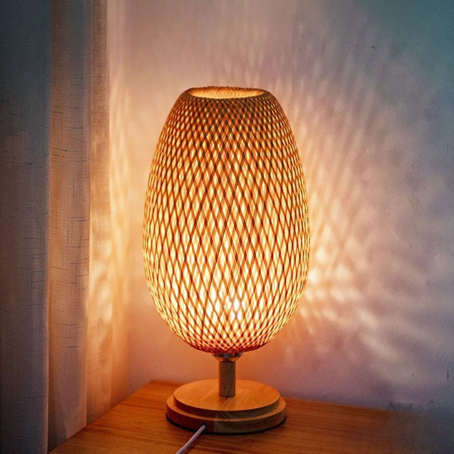 Tall woven bamboo table lamp glowing with warm tricolor light on a wooden surface, casting decorative patterns on the wall — "Woven Glow" Large 18 × 48cm by CL House
