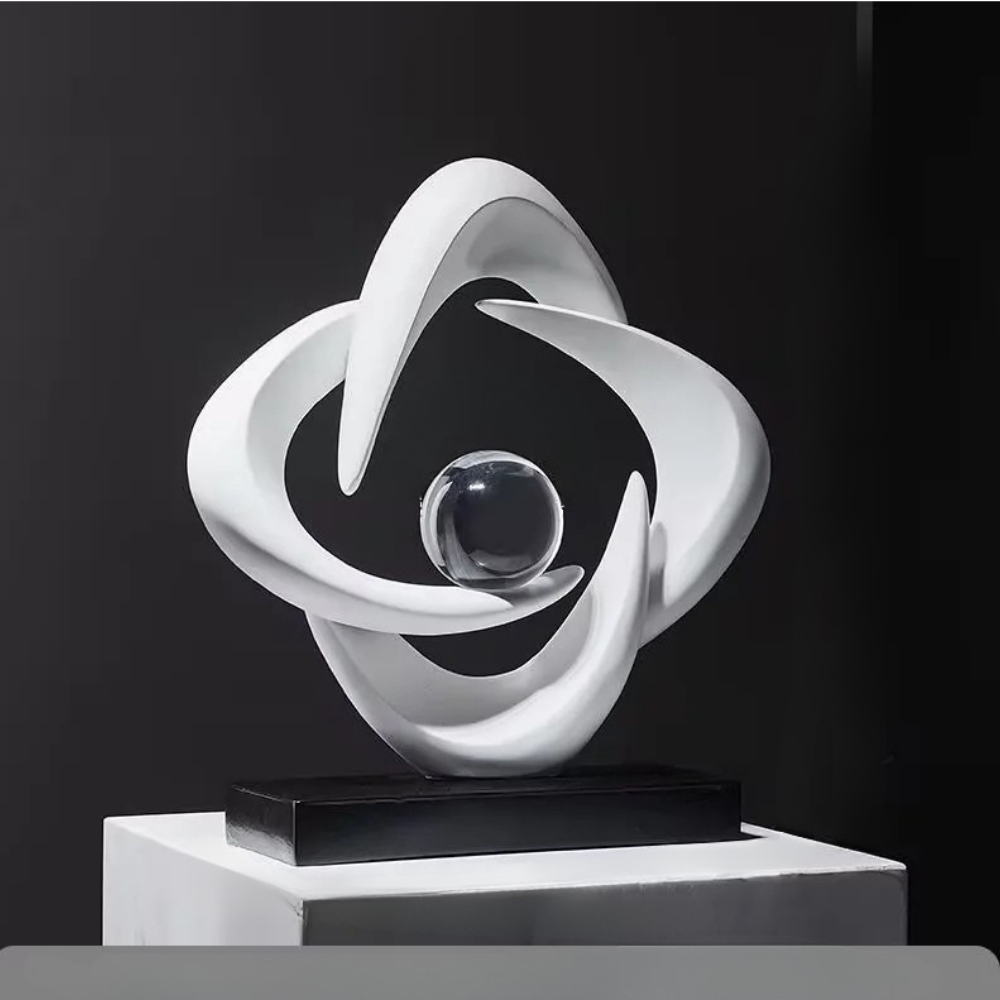 White abstract resin sculpture with three interlocking curved loops and a clear crystal sphere on a black rectangular base, set against a dark backdrop.
