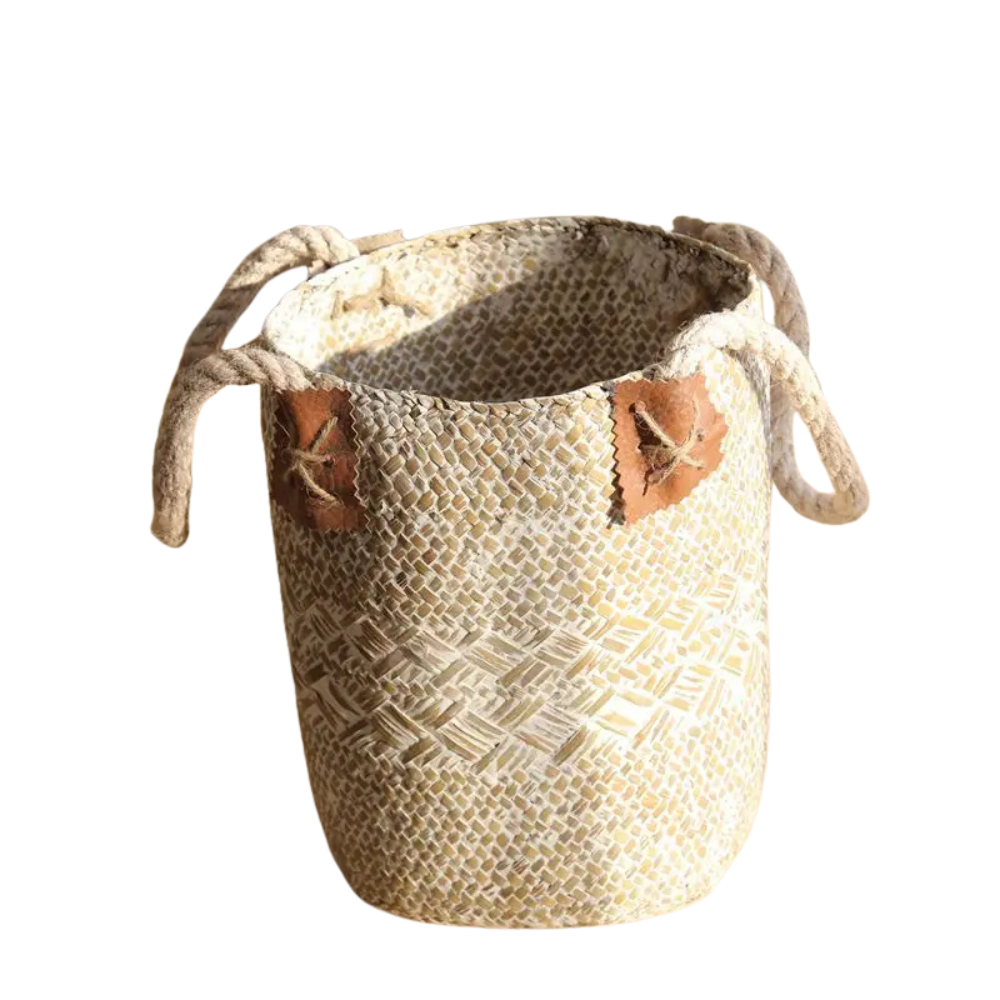 Small white woven straw flower basket vase with rope handles and decorative leaf details displayed on a wooden table.