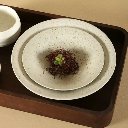 Speckled clay handcrafted ceramic dinner plates in two sizes styled on a dark walnut tray, with dried botanical nest and a small succulent as a centrepiece, and a ceramic bowl alongside