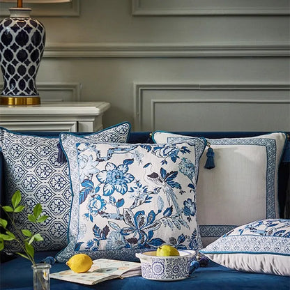 "Blue Willow" chinoiserie linen cushion covers styled on a navy velvet sofa — Blue Garden and Porcelain Frame designs with corner tassels, blue and white ceramic lamp in background — CL House