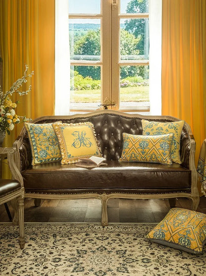 All three "Golden Court" velvet cushion cover designs styled on a Louis XV leather sofa — Golden Monogram at centre, Baroque Lattice lumbar on right and floor, golden curtains and garden window, French country interior