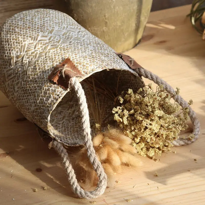 Large white woven straw flower basket vase lying on its side with dried flowers on a wooden table. 
