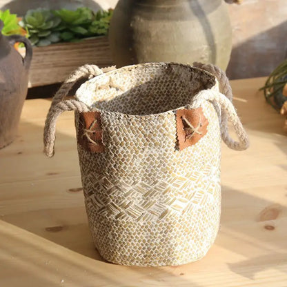 Large white woven straw flower basket vase with rope handles and decorative leaf details displayed on a wooden table.