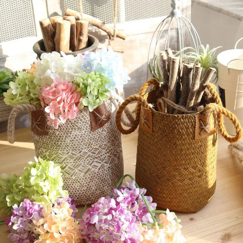 White and natural straw flower basket vases styled with colourful hydrangeas and branches on a wooden table.