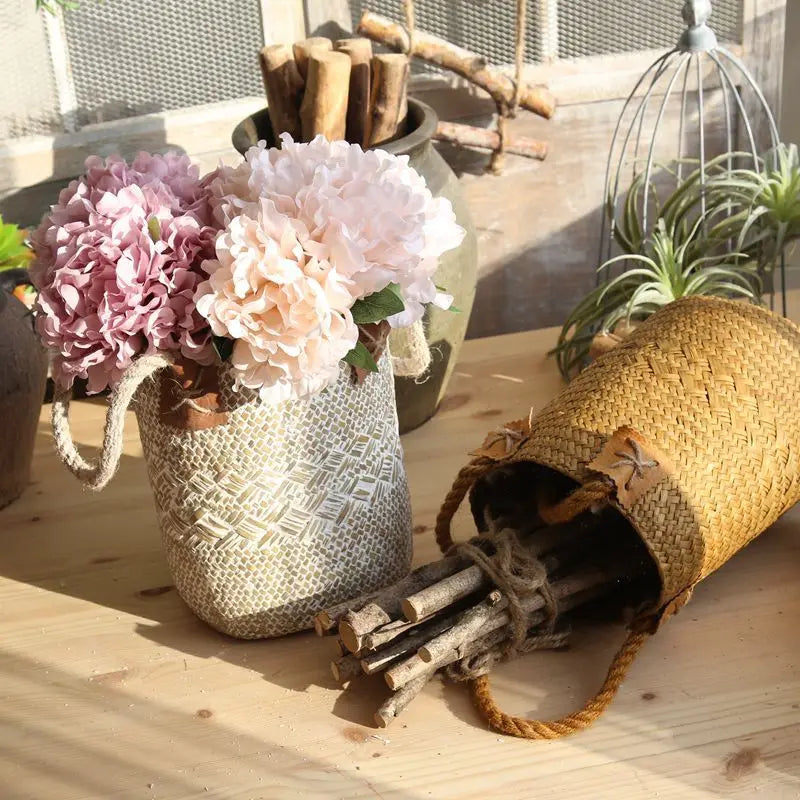 White straw flower basket vase filled with hydrangeas beside a natural straw basket holding wooden stems.