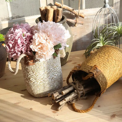 White straw flower basket vase filled with hydrangeas beside a natural straw basket holding wooden stems.