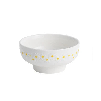"Daisy Bloom" ceramic bowl — front view on white background showing footed base, soft white glaze and raised daisy relief border with golden yellow centres around the rim — product shot