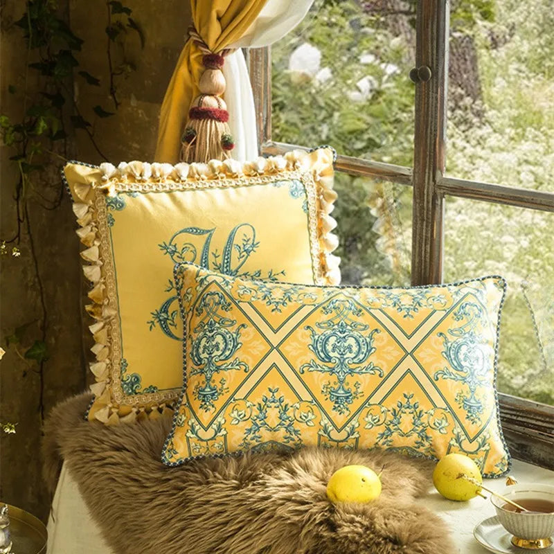  "Golden Court" velvet cushion covers styled on a window seat — Golden Monogram square with ruffled border and Baroque Lattice lumbar, fur throw, lemons and teacup, golden curtain and garden view