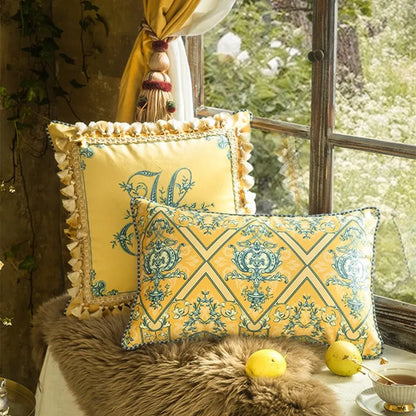  "Golden Court" velvet cushion covers styled on a window seat — Golden Monogram square with ruffled border and Baroque Lattice lumbar, fur throw, lemons and teacup, golden curtain and garden view