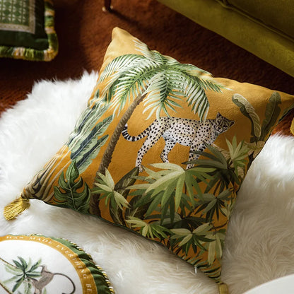  "Wild Kingdom" velvet cushion cover, Savanna Leopard design styled on a white fur throw — ochre velvet with leopard and tropical palms, green velvet sofa and decorative plate in background, gold tassel detail