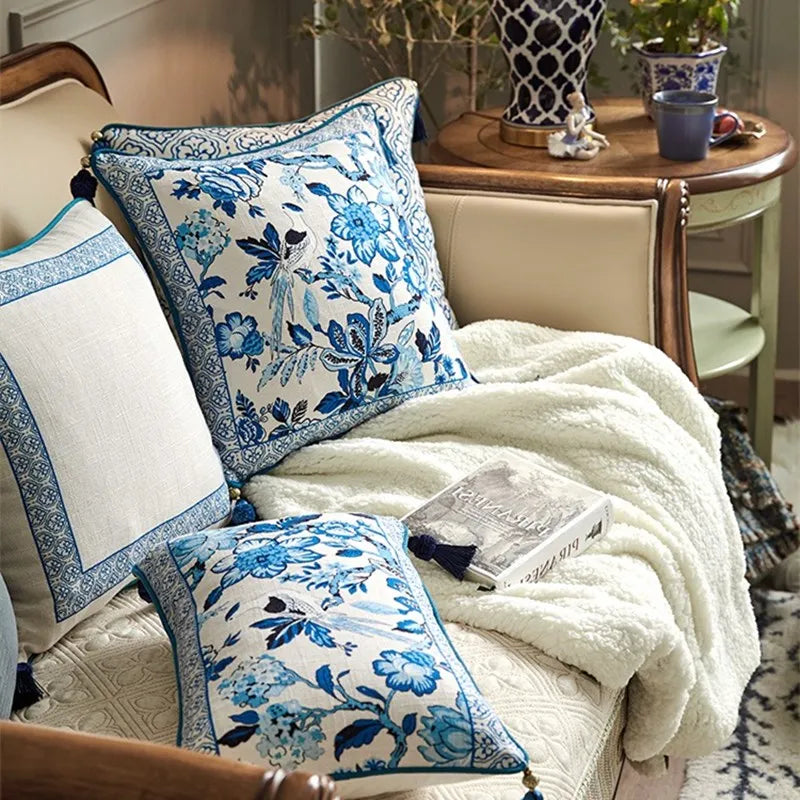 "Blue Willow" chinoiserie linen cushion covers arranged on a textured wool rug — Porcelain Frame, Blue Garden and geometric designs with corner tassels, gold side table in background — CL House