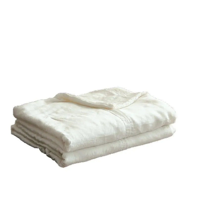  Ivory white quilted linen cotton summer throw blanket, neatly folded on a dark wood bench in a japandi-style interior with wooden shelving and open book