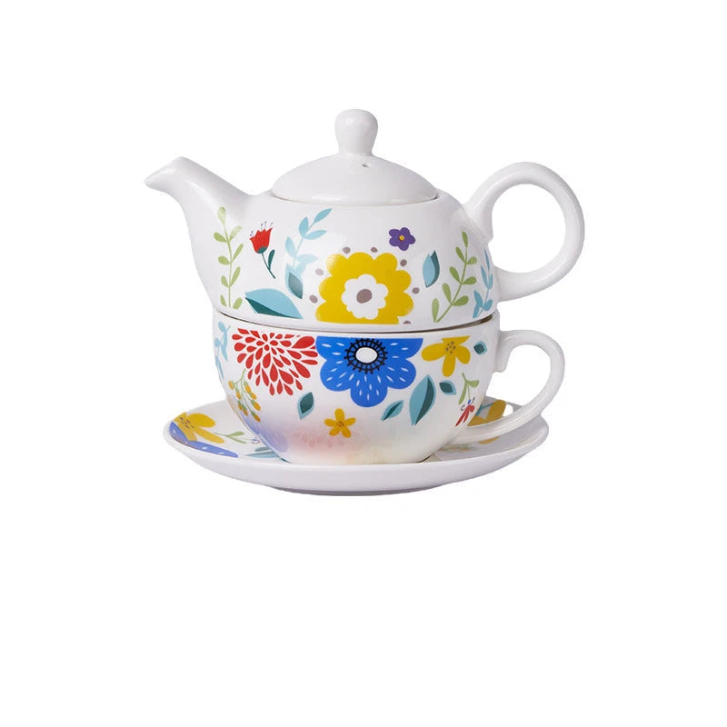 White porcelain tea for one set with vibrant folk-style flowers in red, blue and yellow with teal leaves, teapot stacked on cup and saucer on white background