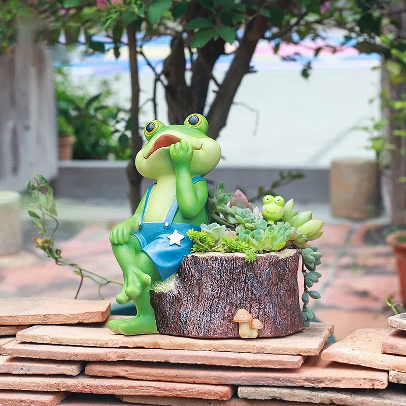 "Frog Tale" resin frog planter — Stump Dreamer styled with succulents and mini frog figurine on a terracotta tile surface in an outdoor garden
