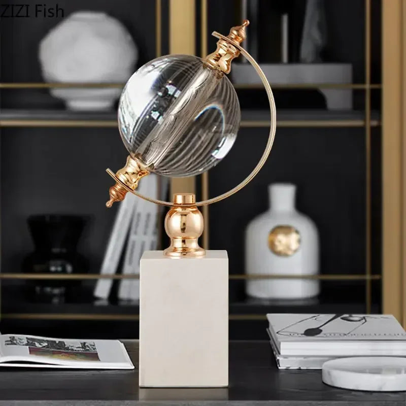 Crystal globe sculpture with gold-plated ring and white marble base, styled on dark shelf with decorative vases and books in luxury interior