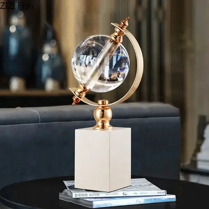 Crystal globe sculpture with gold-plated ring and marble base, styled on coffee table with books in a dark luxury living room setting