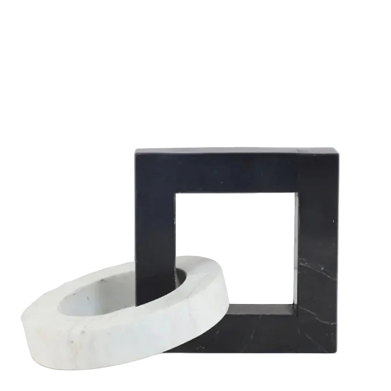 Square black and white interlocking marble sculpture displayed on a light neutral surface against a pale background.