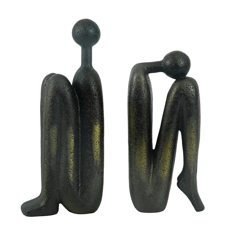 Pair of dark resin abstract human sculptures with elongated forms, shown side by side against a white background.