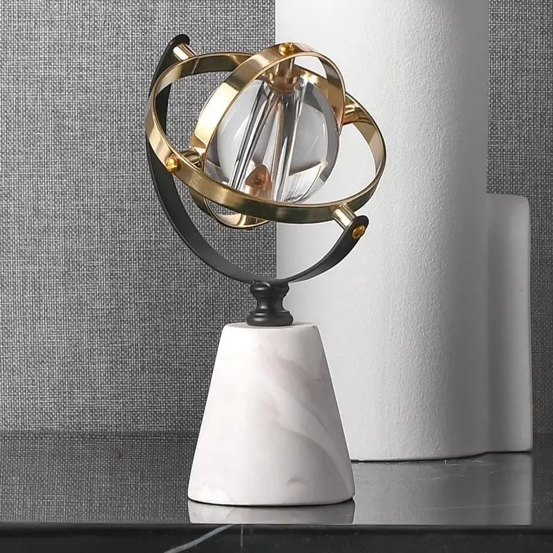 Decorative marble globe with a clear glass sphere and brass and black rings, styled beside a white ribbed vase against a grey textured wall