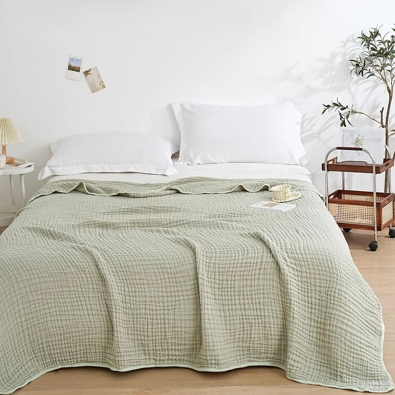  Sage Mist 100% cotton 6-layer muslin throw blanket spread over a bed in a bright minimalist bedroom