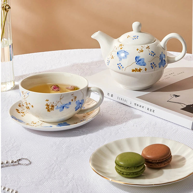 Blue chicory floral porcelain tea for one set styled on a white linen table with brewed herbal tea, macarons and a magazine, warm cosy atmosphere