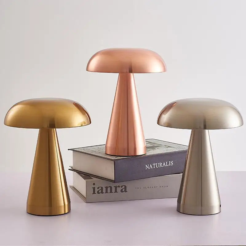 All three Cap & Glow mushroom table lamps displayed together — Golden, Rose Gold and Silver — the Rose Gold elevated on a stack of books, showcasing the full colour range against a soft grey background.