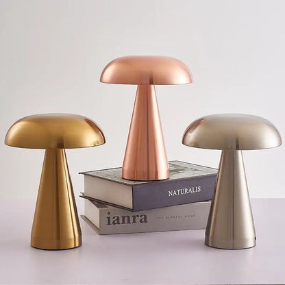 All three Cap & Glow mushroom table lamps displayed together — Golden, Rose Gold and Silver — the Rose Gold elevated on a stack of books, showcasing the full colour range against a soft grey background.