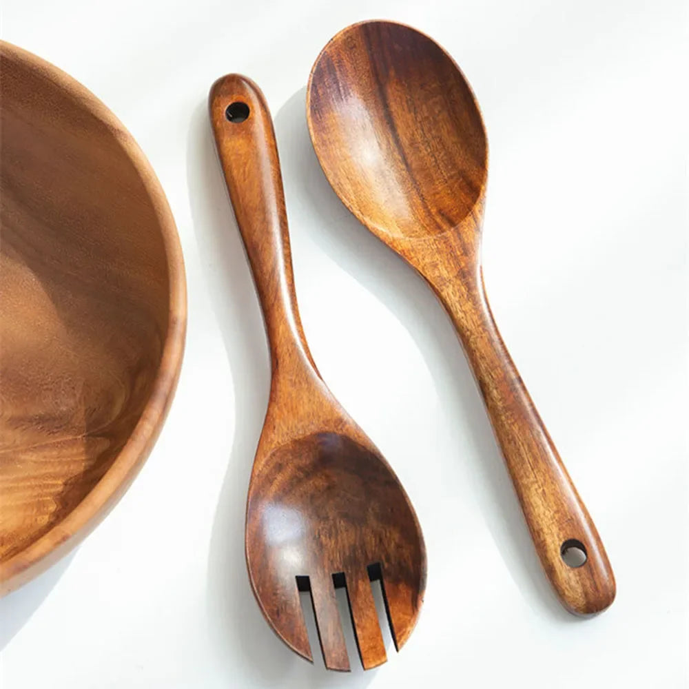 "Wild Harvest" acacia wood salad servers set laid flat beside a wooden bowl, showing serving spoon and salad fork with natural wood grain