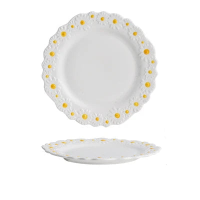 "Daisy Bloom" ceramic small plate — top and profile view on white background showing raised daisy relief border with white petals and golden yellow centres, soft white glaze and scalloped edge — product shot