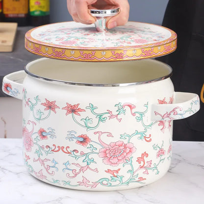 Hand lifting the lid of a floral enamel casserole, Lotus Bloom design — showing cream interior and silver rim, pink lotus print exterior on marble surface — Peony Garden by CL House