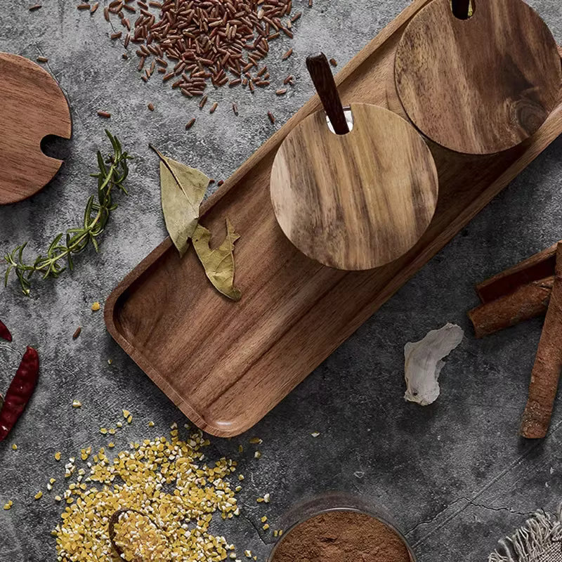  Top view of acacia wood tray with glass spice jars seen from above, surrounded by scattered whole spices — cumin seeds, dried chillies, cinnamon sticks, bay leaves, rosemary and crushed grains — on a grey stone surface, japandi kitchen lifestyle