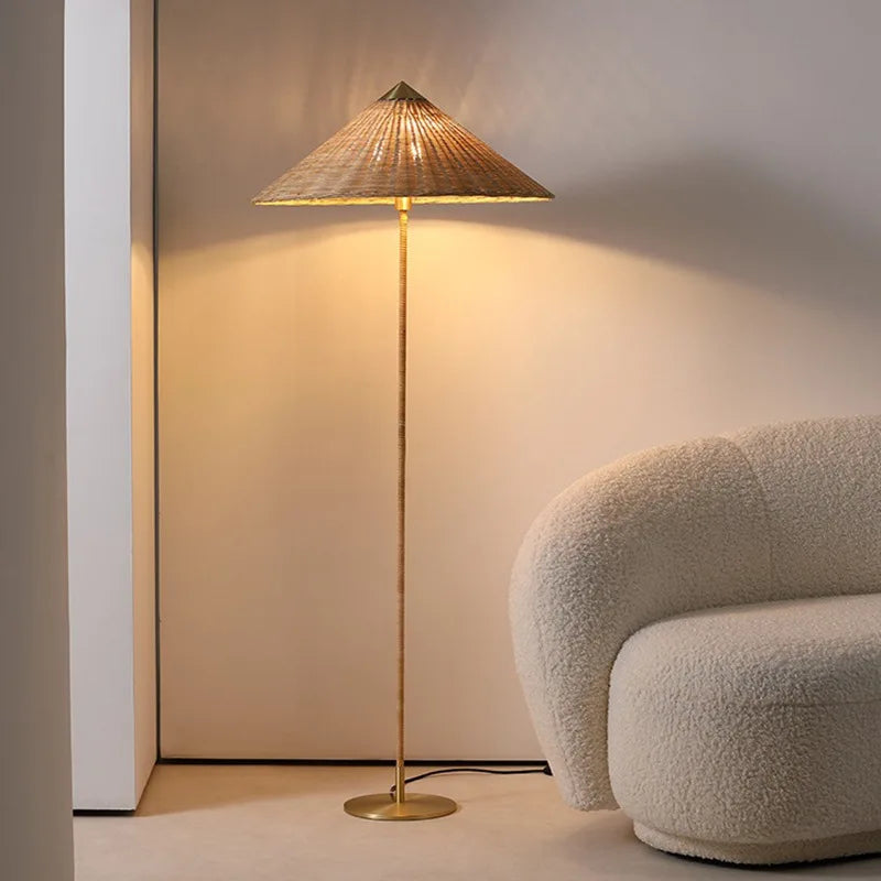  "Cone & Brass" floor lamp with rattan shade glowing warmly in a neutral corner beside a cream bouclé armchair