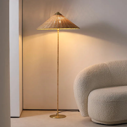  "Cone & Brass" floor lamp with rattan shade glowing warmly in a neutral corner beside a cream bouclé armchair