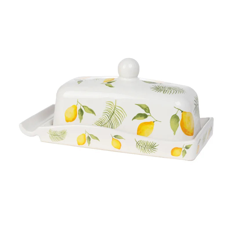 White ceramic butter dish with domed lid, decorated with hand-painted yellow lemons and green fern leaves on a white background.
