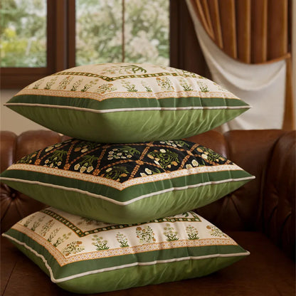 Three Indo-Persian velvet cushion covers stacked on a leather sofa — "Ivory Garden" cream and green botanical print on top and bottom, "Midnight Trellis" black diamond trellis with white florals in the middle, sage green reverse visible on all three — CL House