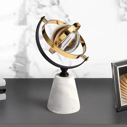 Decorative marble globe with a clear glass sphere and brass and black rings, on a dark desk beside books and a picture frame